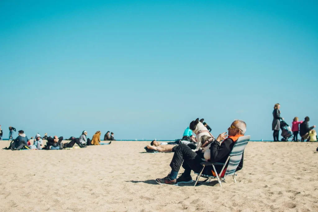 a gentleman sitting on the beach with his dog on his lap