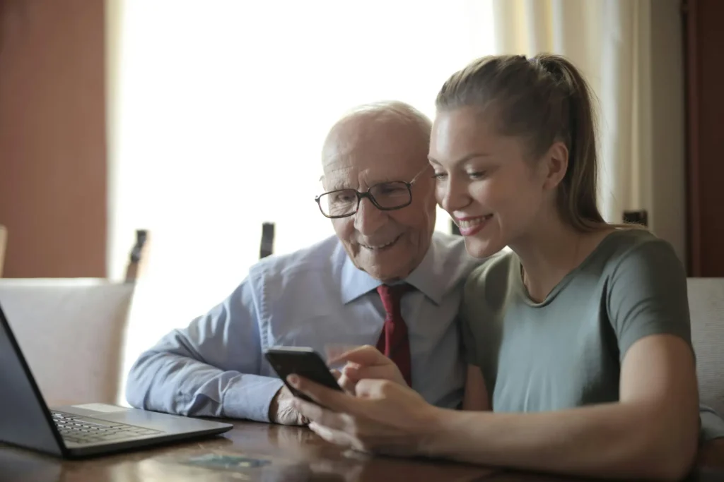 a senior being taught by a younger woman on how to use his cellphone while navigating seniorthrive app