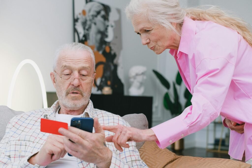 old couple and the man holding a phone while the woman teaches the man to navigate health apps for seniors.
